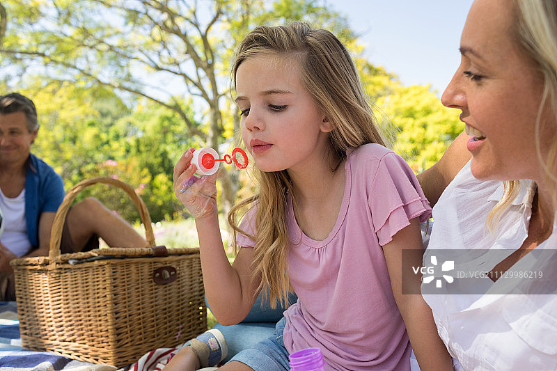 妈妈和女儿在公园野餐时用泡泡棒吹泡泡图片素材