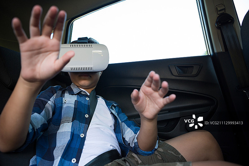 十几岁的男孩在汽车后座上使用虚拟现实耳机图片素材