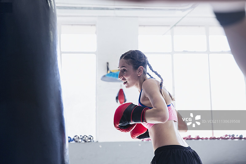 坚定的年轻女拳击手拳击在拳击袋在健身房图片素材