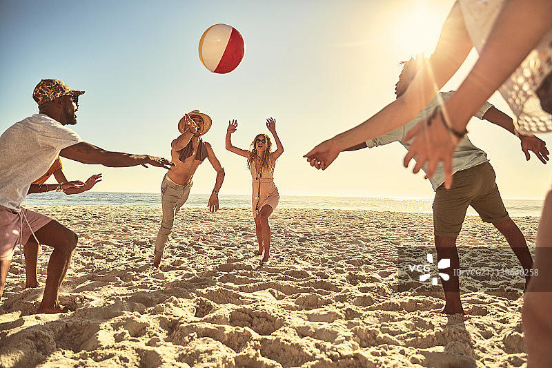 顽皮的年轻朋友在阳光明媚的夏日沙滩上玩沙滩球图片素材