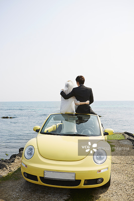 新婚夫妇坐在海滩附近的黄色汽车上图片素材