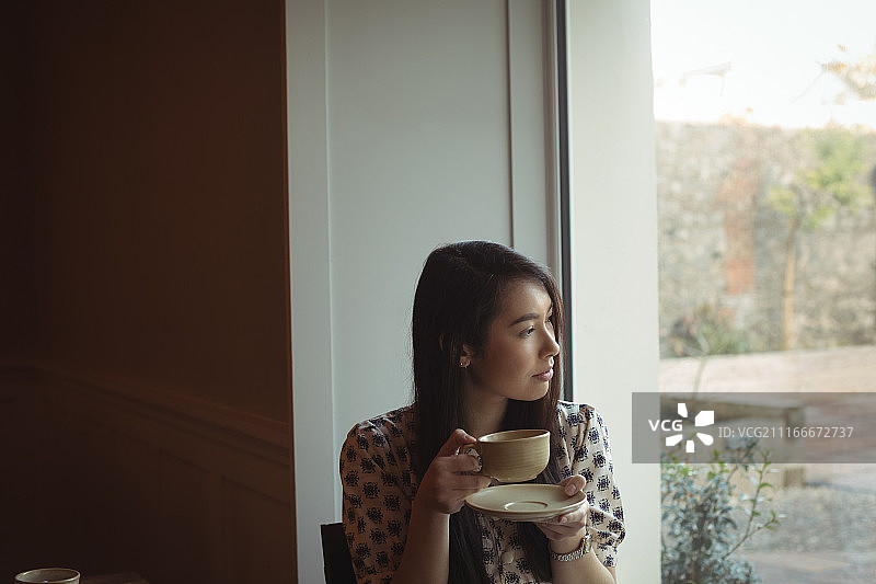 Woman having cup of coffee near window at caf茅图片素材