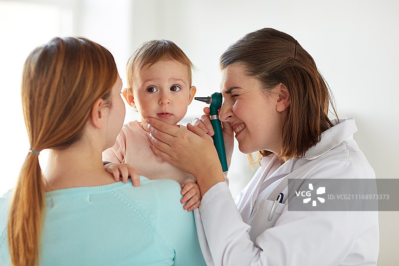 医学、保健、儿科和人们的概念-耳鼻喉科医生或医生检查婴儿耳朵用耳镜和年轻妇女在诊所。医生在诊所用耳镜检查婴儿的耳朵图片素材