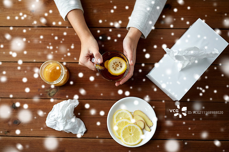健康、传统医学和民族科学概念——病妇用柠檬、蜂蜜和生姜和纸擦茶盒，放在木桌上盖上雪。生病的女人喝柠檬和姜茶图片素材