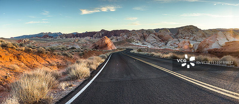 在金色的暮色中，一条柏油路蜿蜒穿过沙漠和群山图片素材