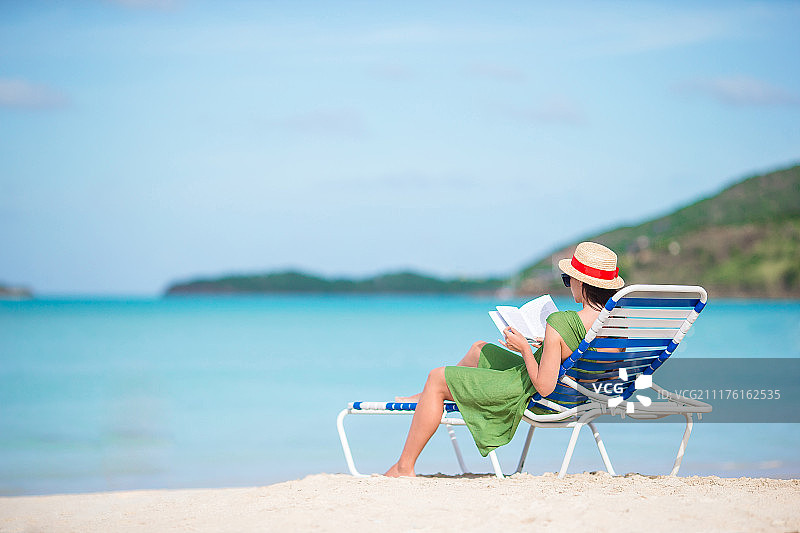 年轻女子在沙滩上的躺椅上看书图片素材