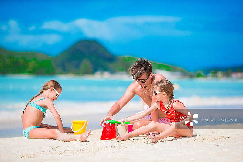 父亲和两个女孩在沙滩上玩沙子图片素材