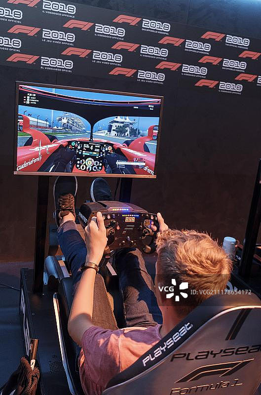 在欧洲德国科隆，北莱茵-威斯特伐利亚州的计算机和视频游戏展上，游客在驾驶模拟器F1 2018的屏幕前玩电脑游戏图片素材