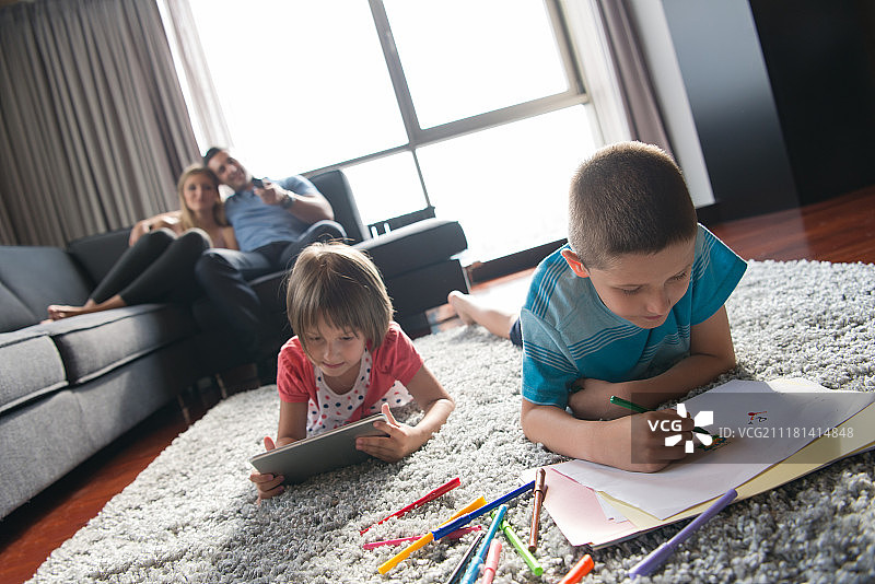 快乐的年轻家庭一起玩在家里的地板上使用平板电脑和儿童绘画集图片素材