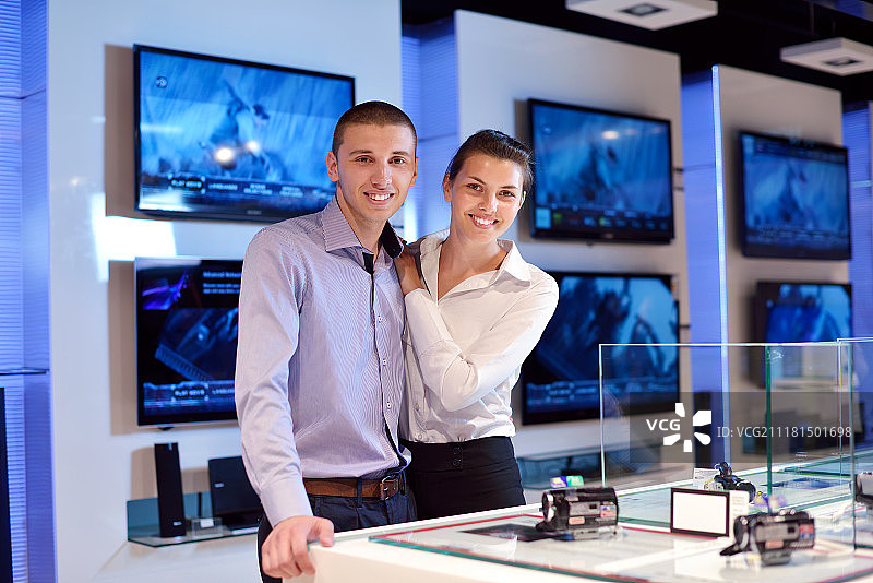 年轻夫妇在消费电子商店看最新的笔记本电脑，电视和相机购买图片素材