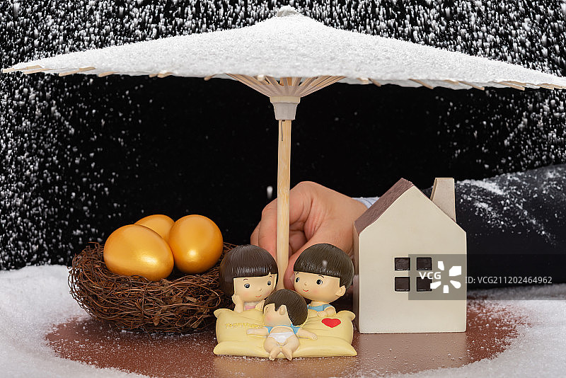 商务人士用伞给年轻的一家三口及金蛋和房子遮挡风雪家庭保障规划图片素材