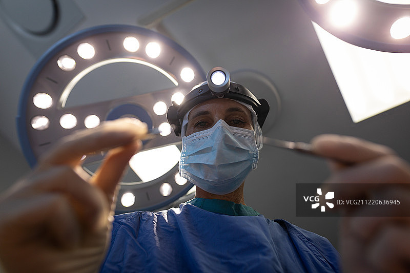 一个成熟的白人女性外科医生在开始手术前拿着手术器械的低角度视图图片素材
