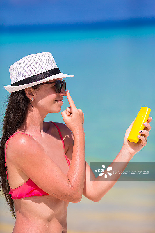 年轻快乐的女人在白色的海滩上用防晒油在她的鼻子上图片素材