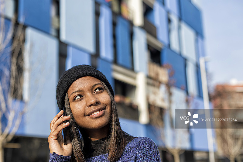 一个快乐的年轻非洲妇女站在户外打电话的肖像，而…图片素材