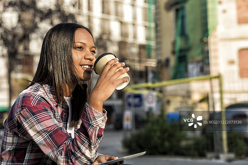 年轻美丽的非洲裔美国妇女坐在户外的城市与平板电脑图片素材