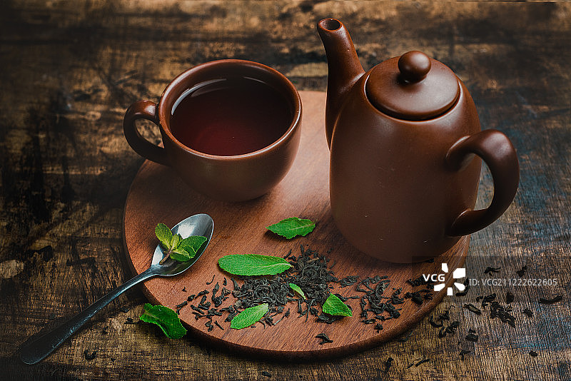 薄荷茶在棕色的陶瓷杯和茶壶上，在温暖的木制背景与茶和薄荷叶冲泡图片素材