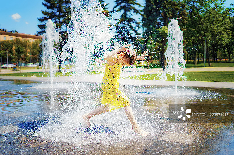 穿着黄色衣服的女孩在喷水池里玩得很开心图片素材