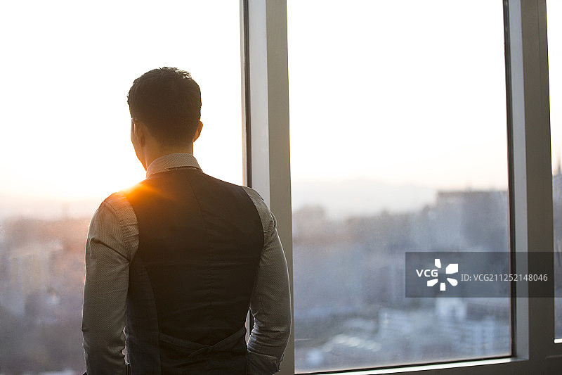 一个成功男商务人士站在办公大厦玻璃窗前思考工作看风景图片素材