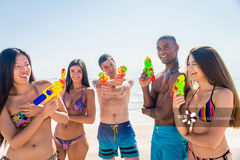 一群快乐的朋友摆着水枪在海滩上图片素材