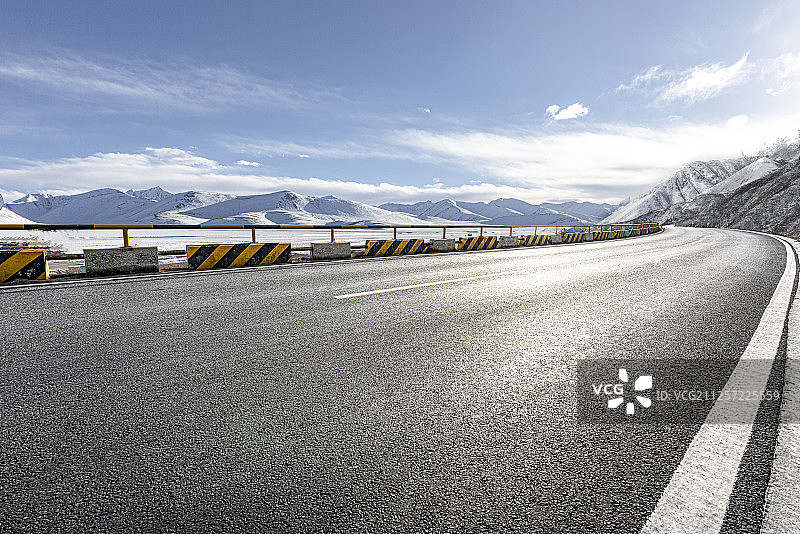 高原雪山前弯曲的柏油路面和洁净的天空图片素材