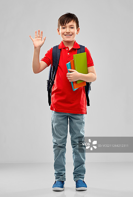 学校，教育和人的概念-微笑的小学生男孩在红色马球t恤在眼镜与书和袋挥舞在灰色的背景。微笑的学生男孩与书和书包图片素材