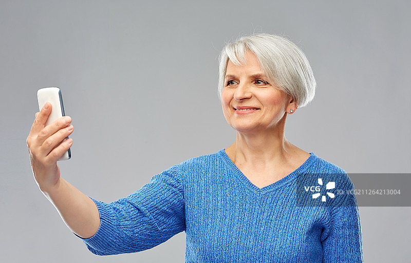 科技和老年人概念-微笑的高级女性在灰色背景下用智能手机自拍。微笑的高级女性用智能手机自拍图片素材