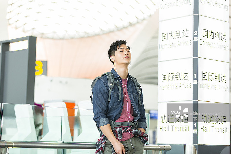 青年男子背着旅行包拿着手机戴耳机听音乐在机场休息放松等候飞机起飞图片素材