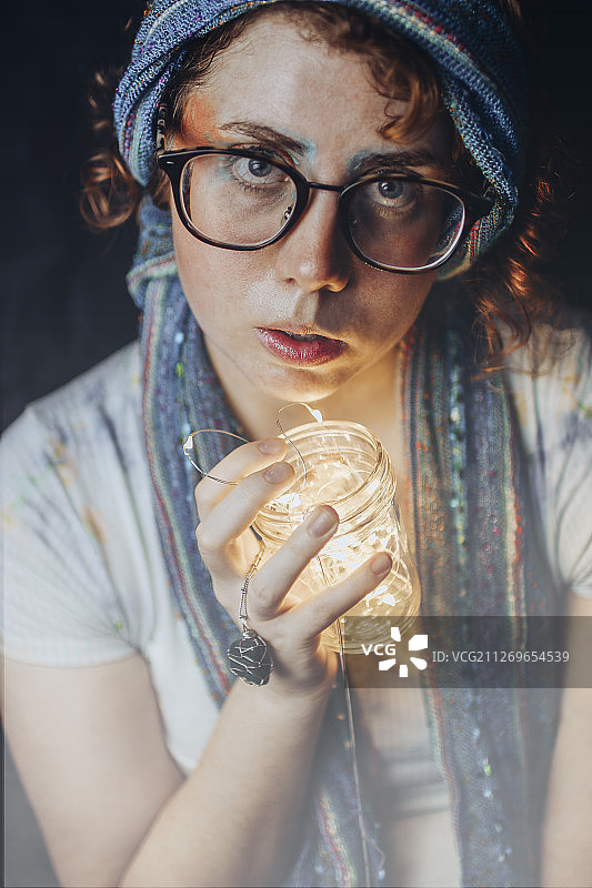 中年女巫的大头照片戴着眼镜和头巾，拿着闪亮的玻璃物体图片素材