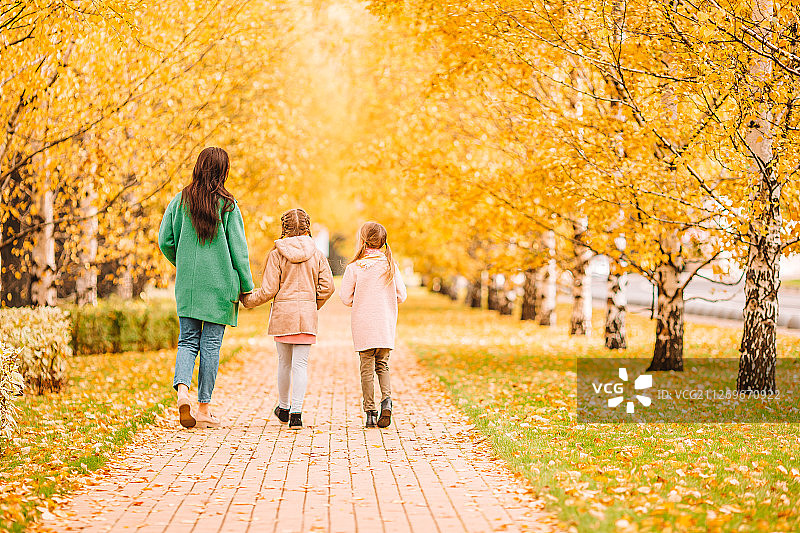 母亲和两个女儿手牵着手在秋天的公园里散步图片素材