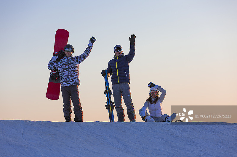 夕阳下三个青年男女在滑雪场挥手欢呼图片素材
