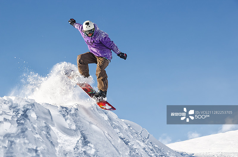 戴着头盔和面具的时尚滑雪板从高雪坡上跳下来图片素材