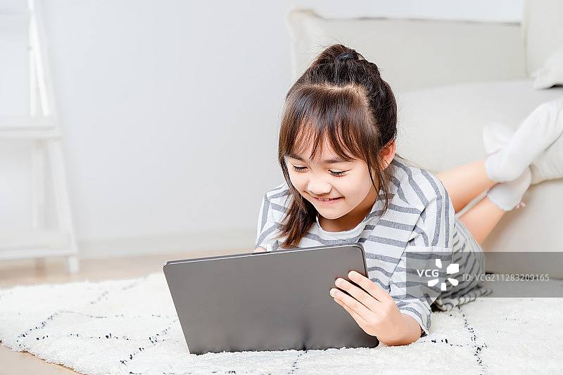 趴在地毯上玩平板电脑的亚洲小女孩图片素材
