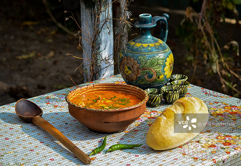 罗马尼亚:传统餐具(瓷壶、水杯、木碗)，桌上放面包、汤和青椒图片素材