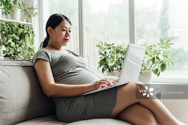 一位年轻的亚洲孕妇正在使用电子设备图片素材