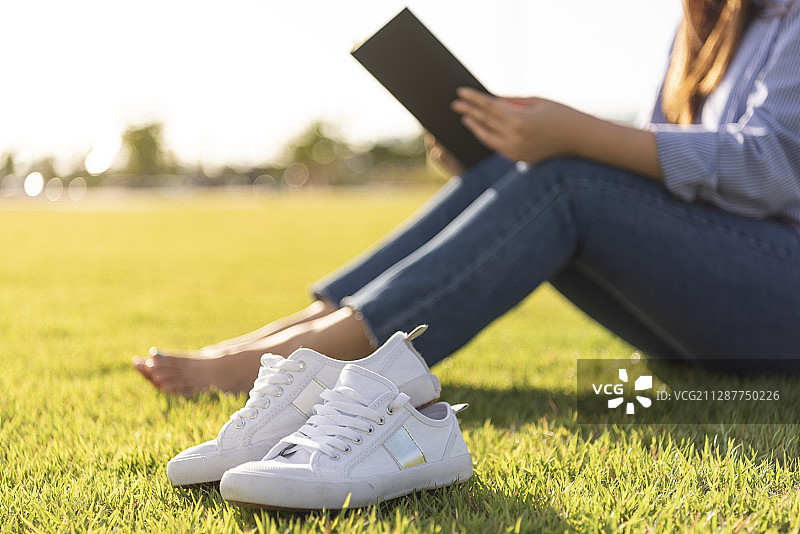 女人赤脚坐在草地上看书的照片图片素材