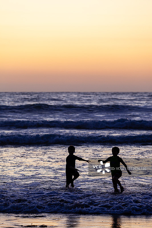 黄昏下两个孩子在海边玩耍图片素材