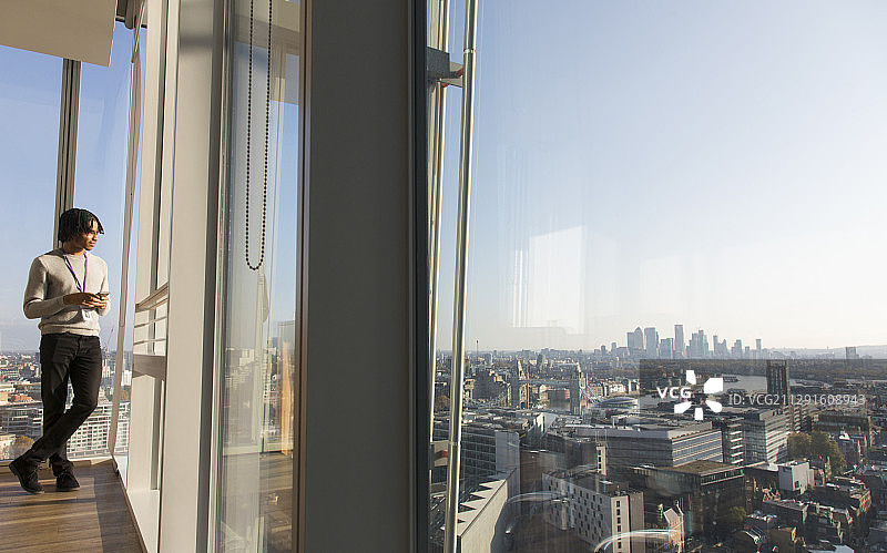 商人站在阳光明媚的城市高层办公窗口图片素材