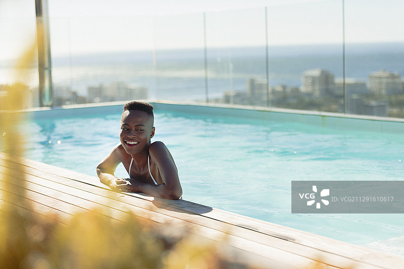 快乐的年轻女子在阳光明媚的豪华游泳池里图片素材
