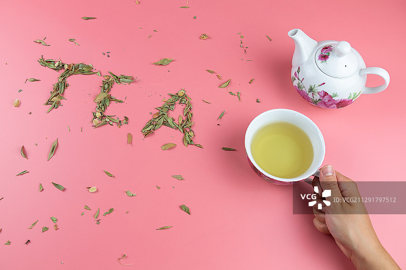 在粉红色的背景上，用茶壶和握着茶杯的人的手拼出单词Tea图片素材