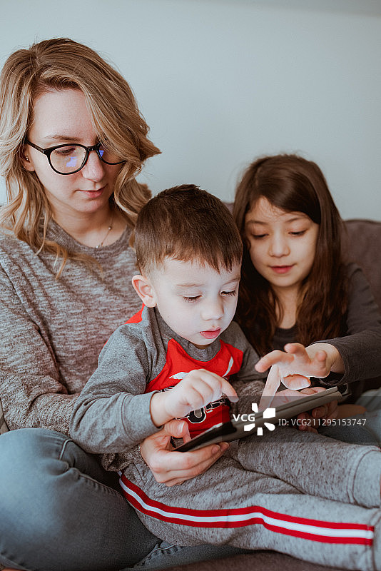 加拿大温哥华，母亲，女儿和儿子坐在家里的沙发上使用数字平板电脑图片素材
