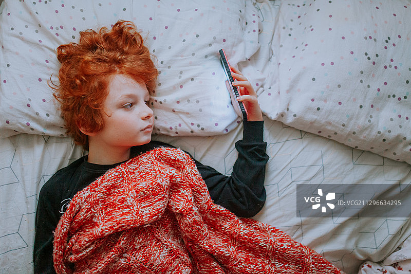 加拿大维多利亚，一名红发男孩在床上用智能手机阅读图片素材