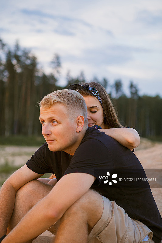 俄罗斯特维尔，一对年轻夫妇坐在沙滩上拥抱的侧视图图片素材