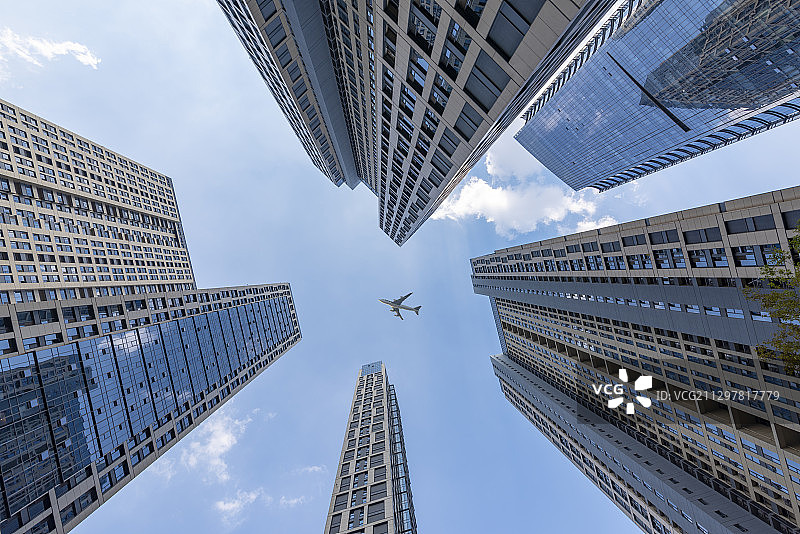 仰拍视角高楼大厦中飞过的一架飞机图片素材