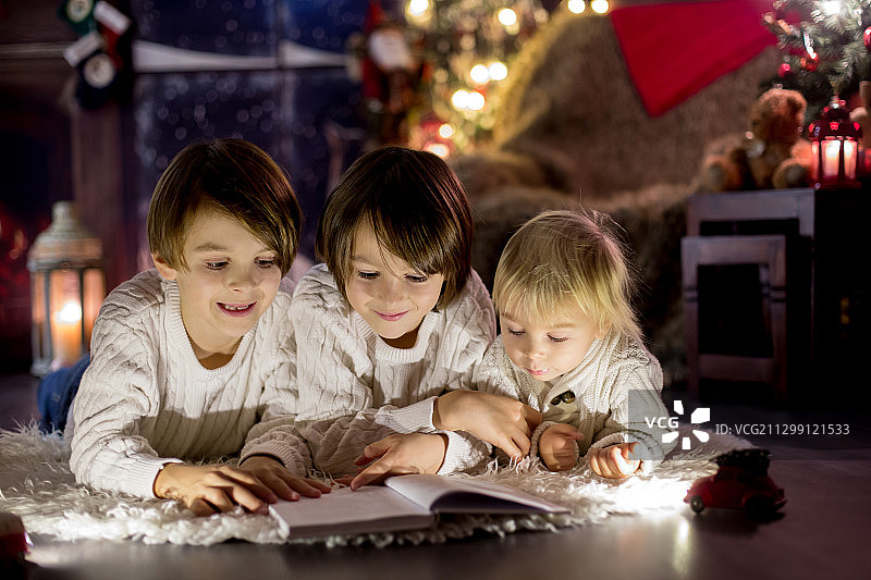 三个孩子，男孩兄弟，在圣诞节晚上在家读书图片素材