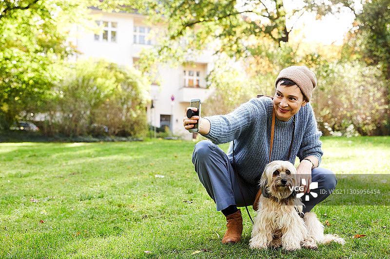 一个中年妇女在公园里和她的小狗在秋天自拍的肖像图片素材