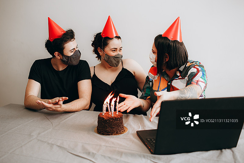 巴西米纳斯吉拉斯州贝洛奥里藏特，年轻的成年人朋友们一起庆祝生日，戴着面具，用笔记本电脑上网图片素材