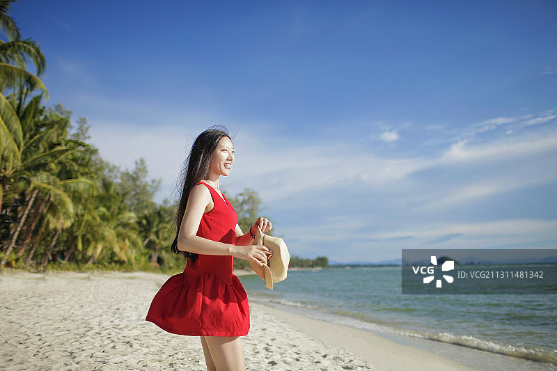 穿红裙的亚洲女子走在海边图片素材
