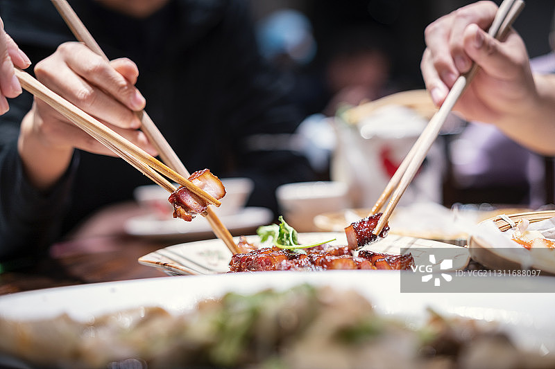 几个人用筷子夹餐桌上的蜜汁叉烧图片素材