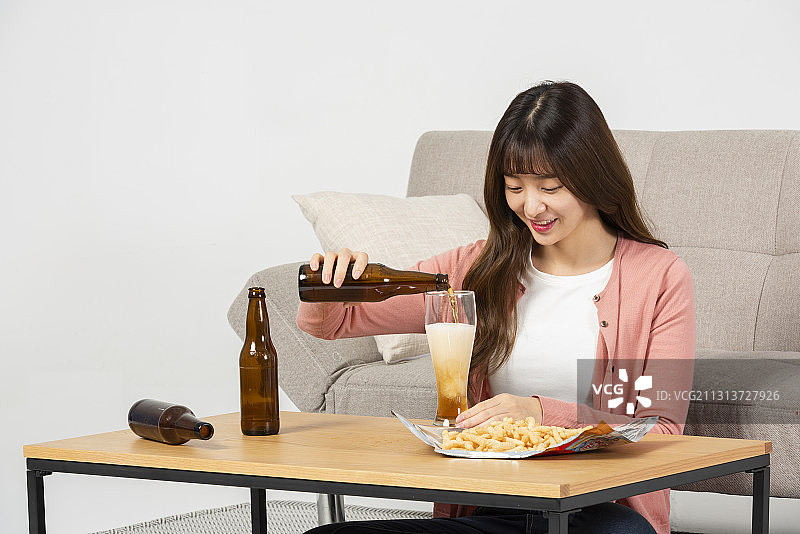 女人坐在桌边喝着啤酒，在沙发前吃着零食，看起来很担心图片素材