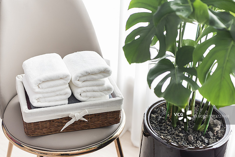 叠好的毛巾放在花盆和窗帘旁边的椅子上的篮子里图片素材